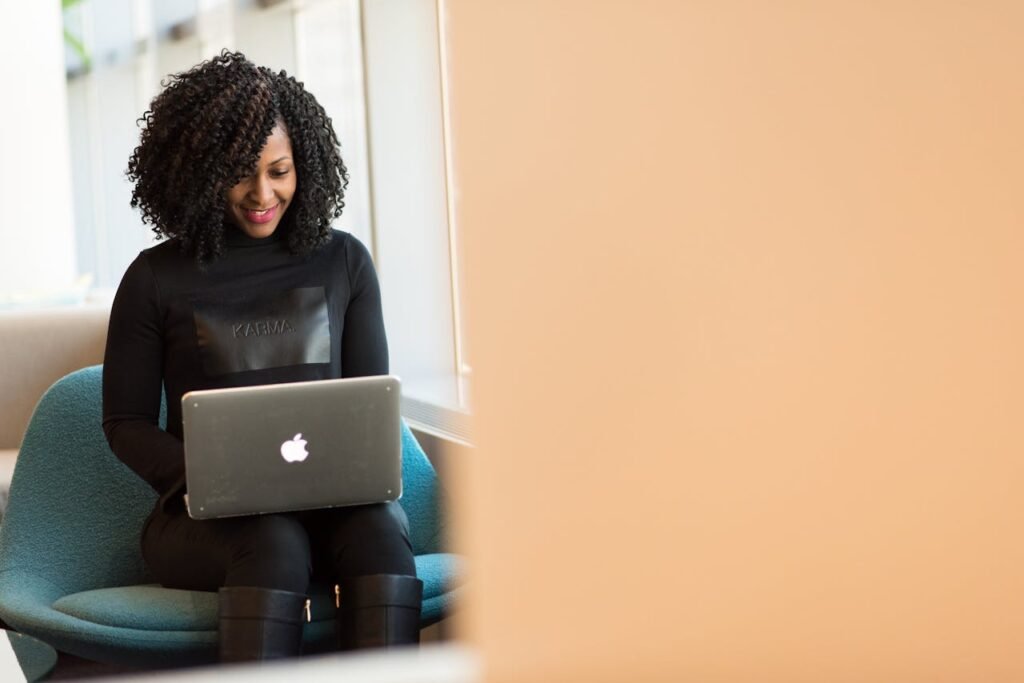 African American woman happily working on a laptop in a modern office setting.
